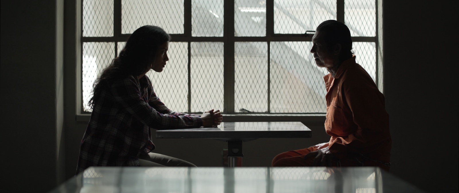 Prison visiting room in Avenge the Crows, two figures at a table silhouetted against a barred window