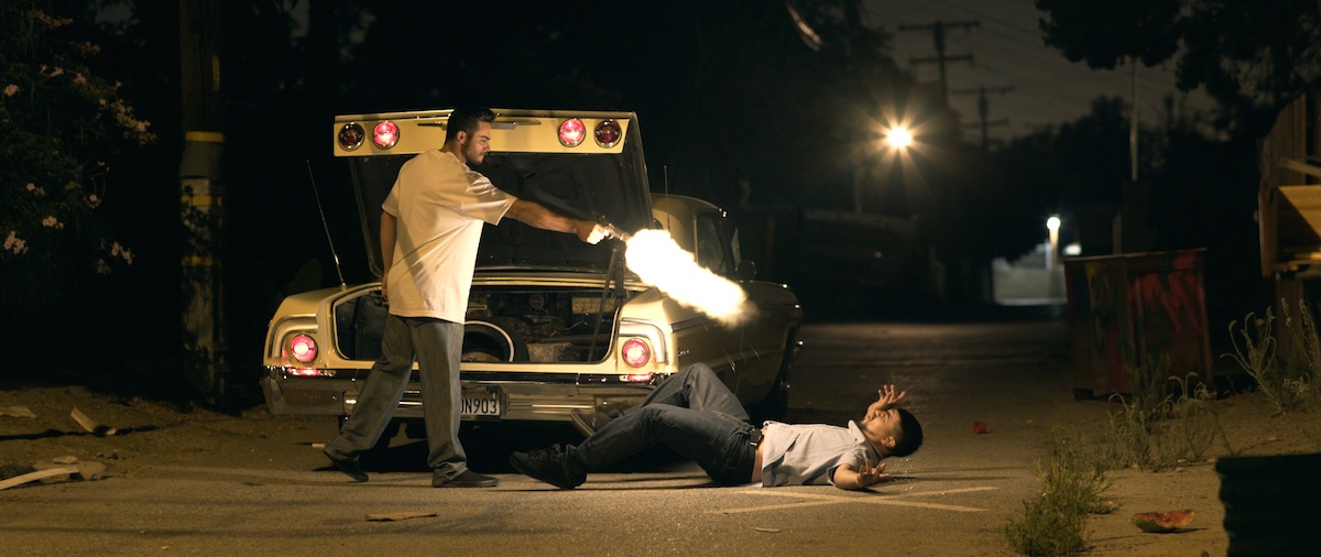 Night street shootout in Avenge the Crows, muzzle flash beside a car with a body on the asphalt