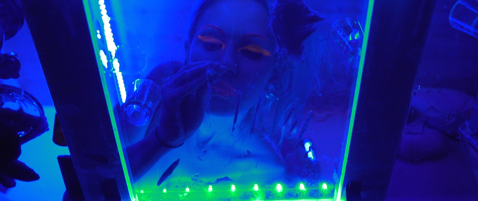Character behind a green and blue lit glass tank in Avenge the Crows