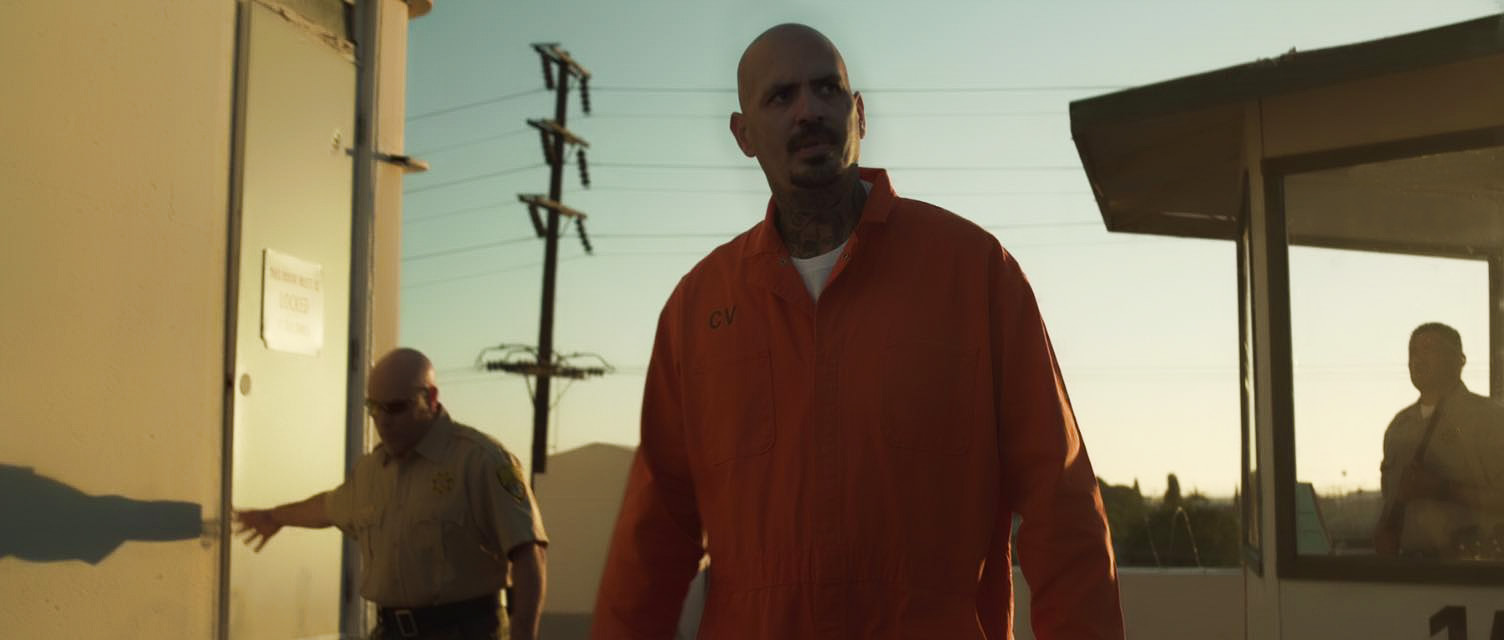 Man in an orange prison jumpsuit outdoors at sunset in Avenge the Crows