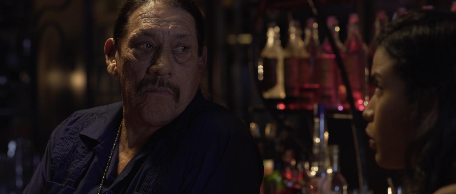 Older man at a dimly lit bar lined with bottles in Avenge the Crows