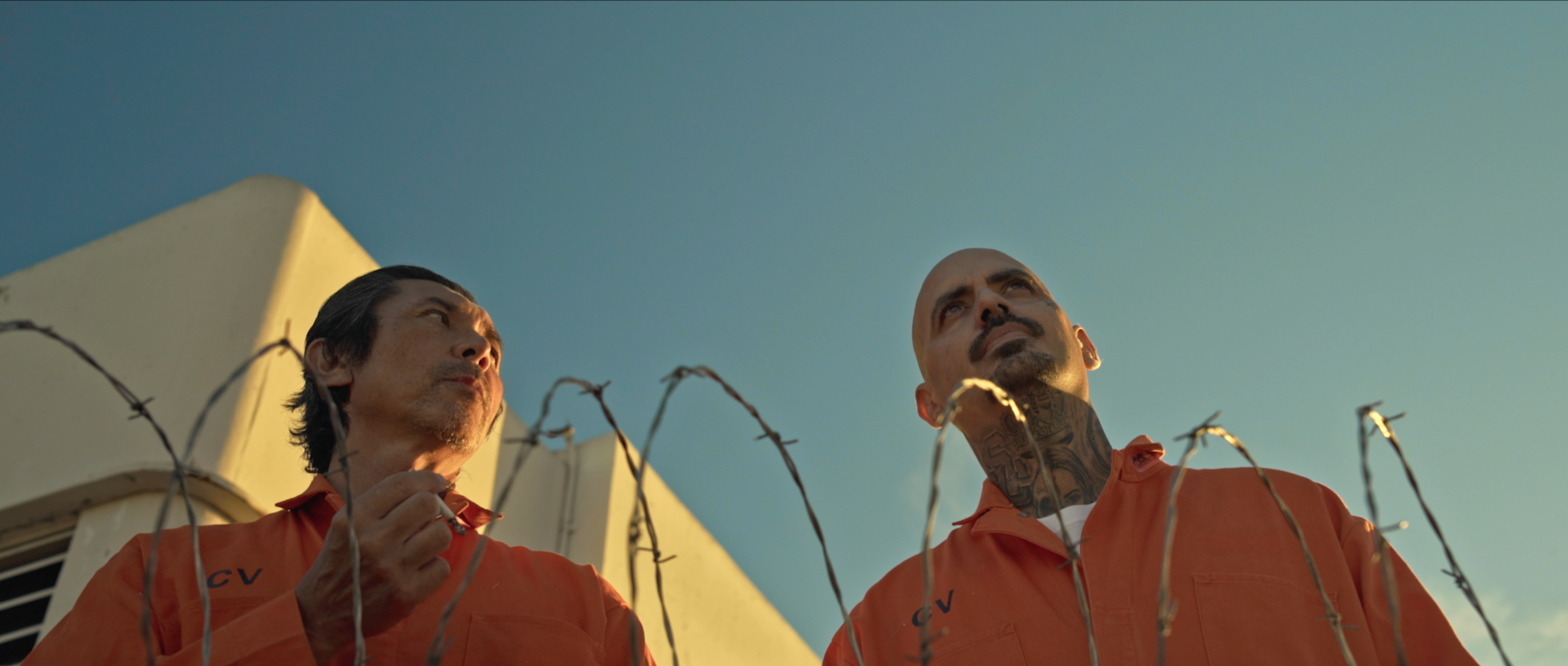 Two inmates in orange jumpsuits in the prison yard beneath white tents, Avenge the Crows