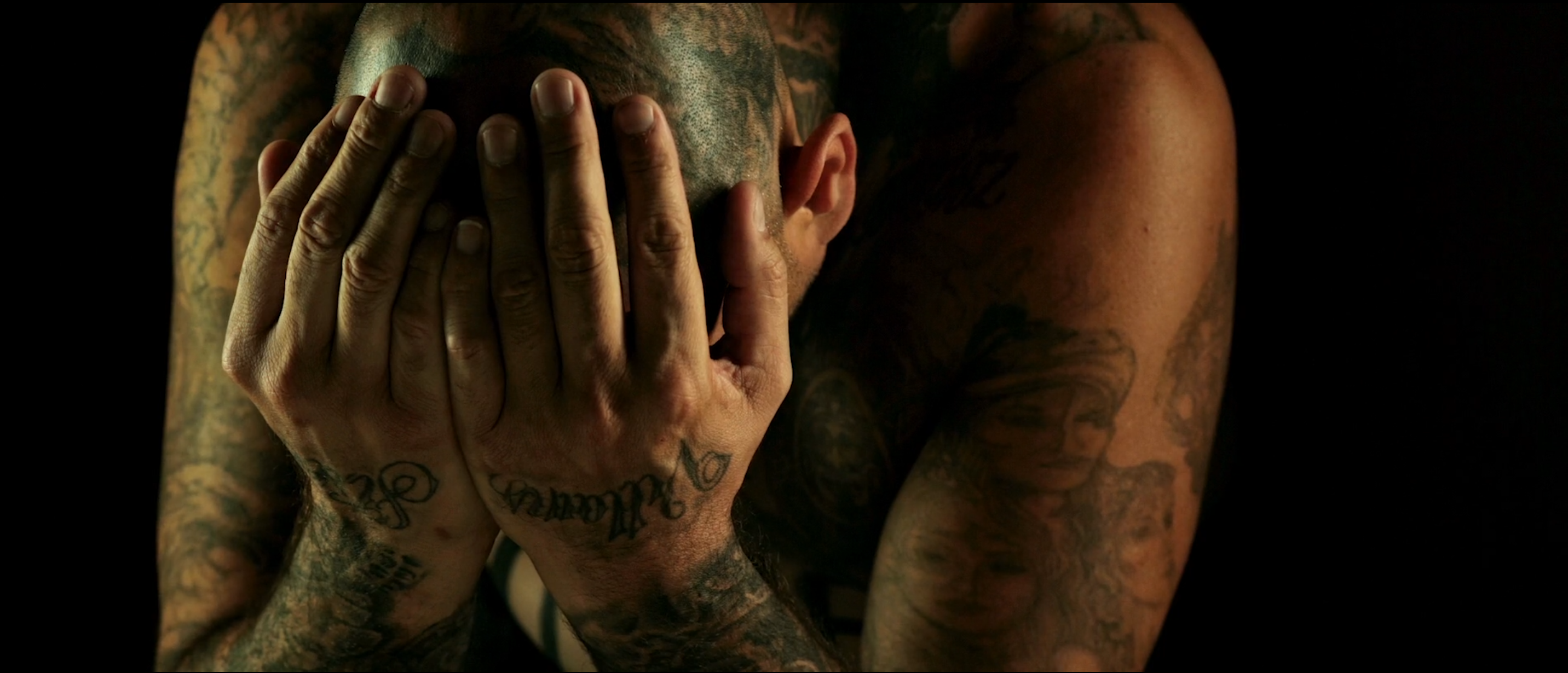 Heavily tattooed character with his hands over his face in Avenge the Crows