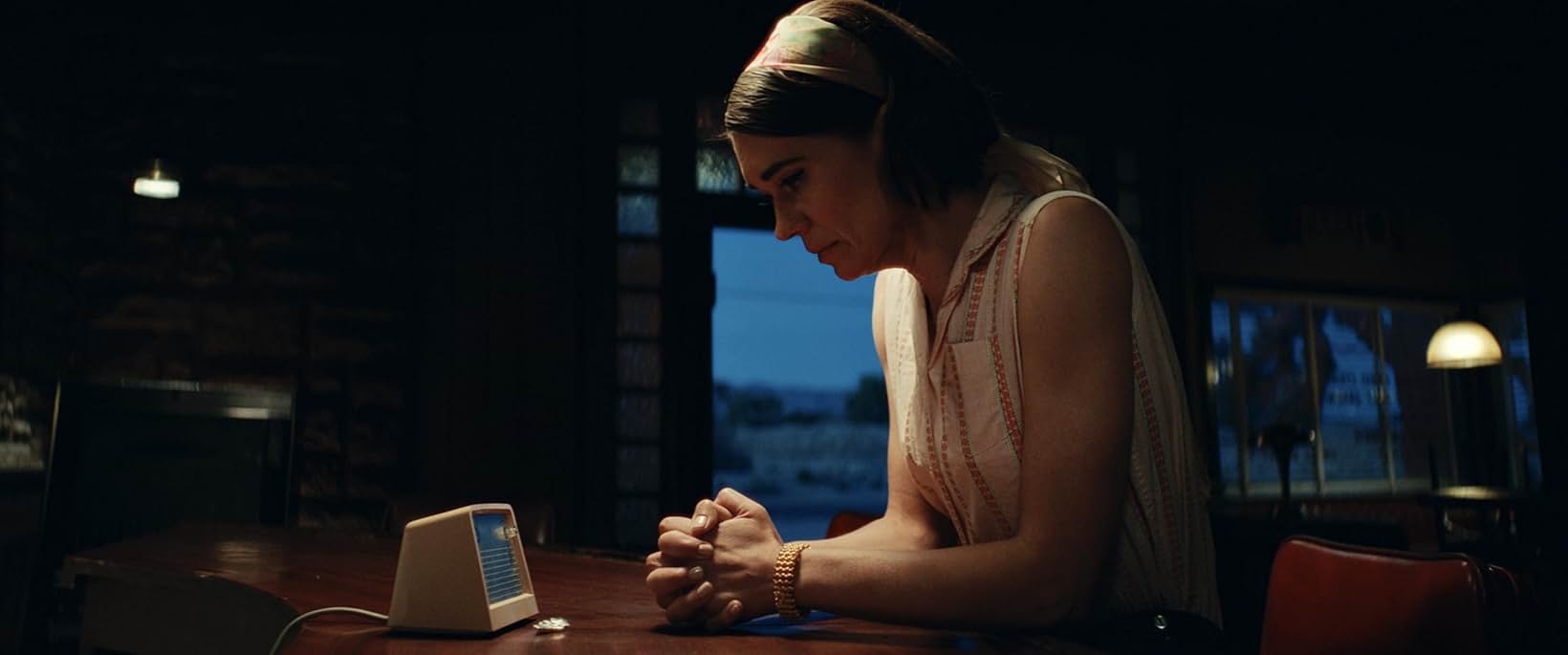 Character at a table with a period radio set in a darkened room, Edge of Space