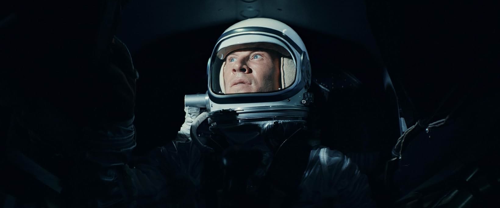 Pilot in a silver pressure suit and helmet lit against darkness, Edge of Space