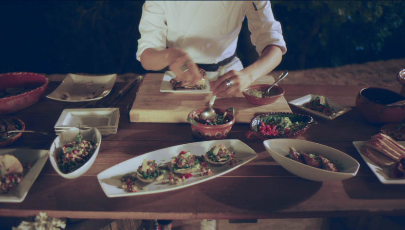 Hands plating food across a rustic wooden table, food styling and production design for In Other Words