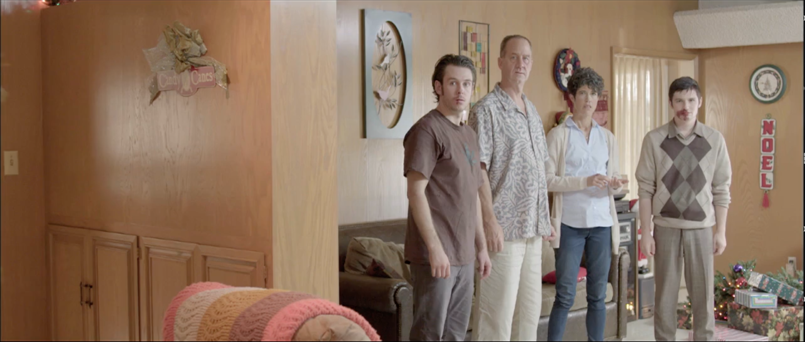 Family of five in a wood-panelled 1970s living room hung with NOEL letters, Takanakuy