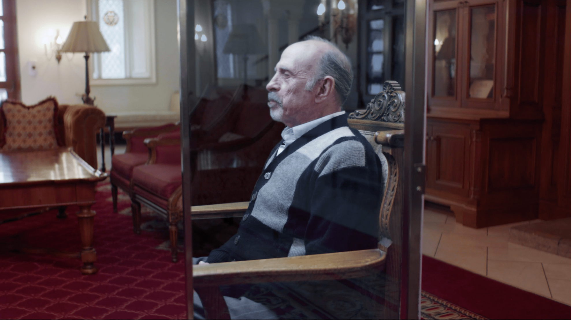 Older man seated in a formal red-carpeted room with period furniture, The Liberator