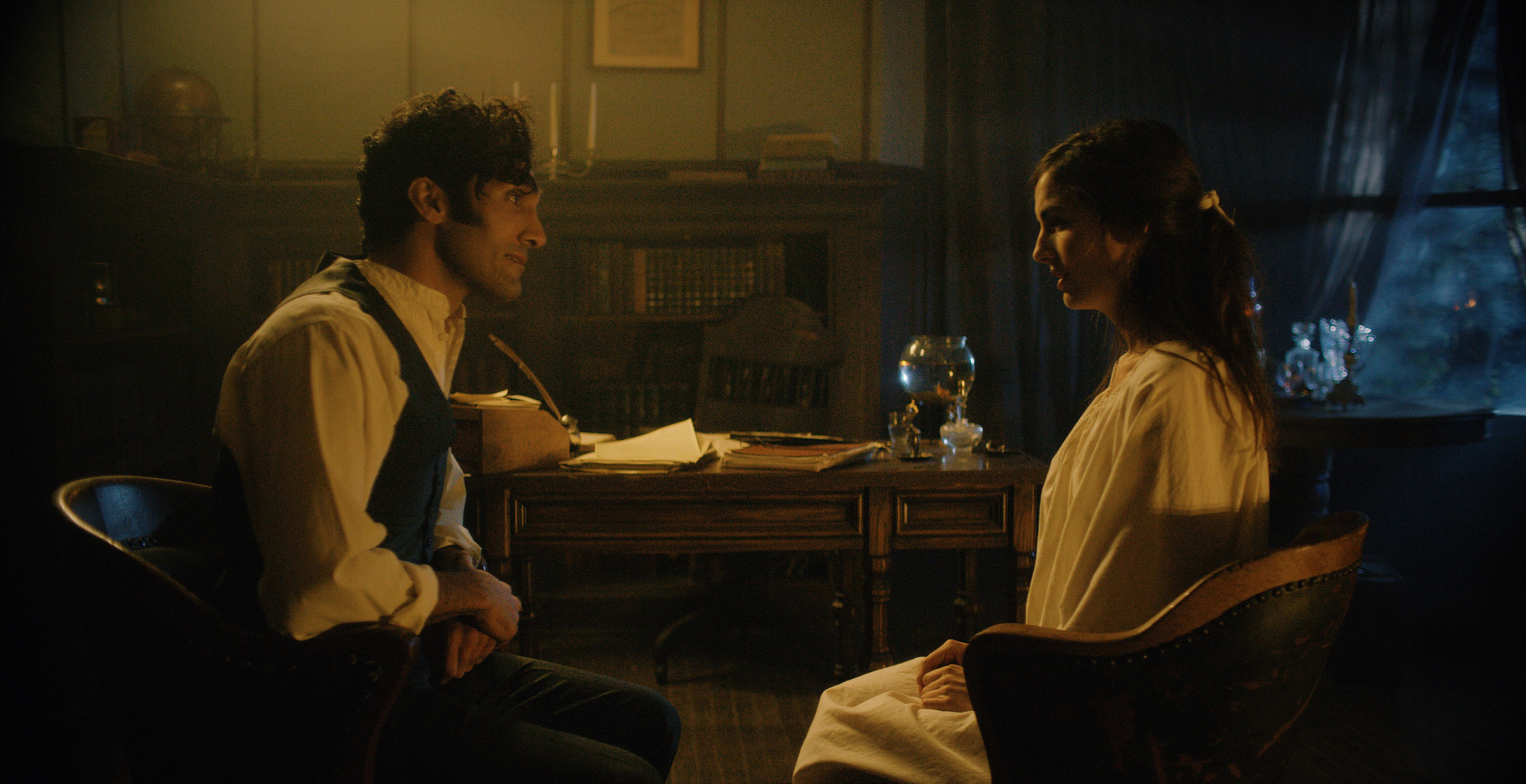 Two characters at a small table beside a window in warm lamplight, period interior from The Mad Whale