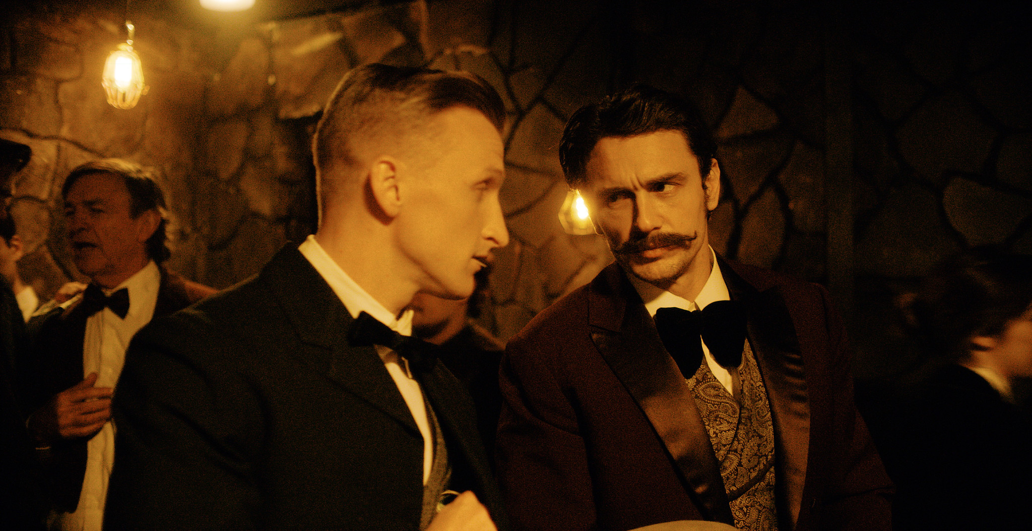 Two men in Victorian waistcoats in close conversation beside a stone wall, The Mad Whale