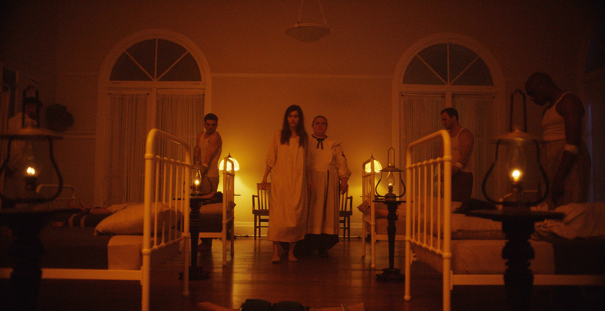 Asylum dormitory at night in The Mad Whale, rows of iron beds and patients in white gowns lit by candles