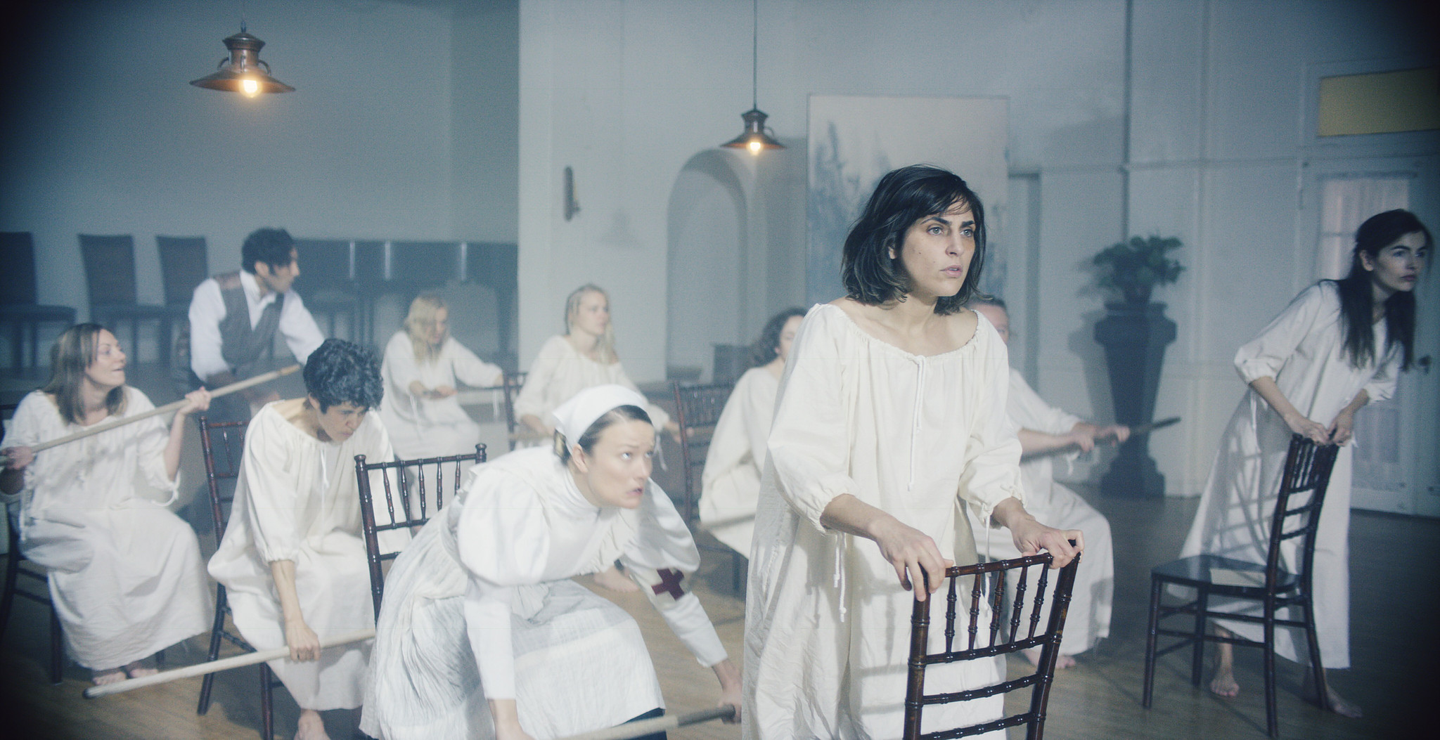Patients and nurses seated on wooden chairs in a bright asylum hall, The Mad Whale