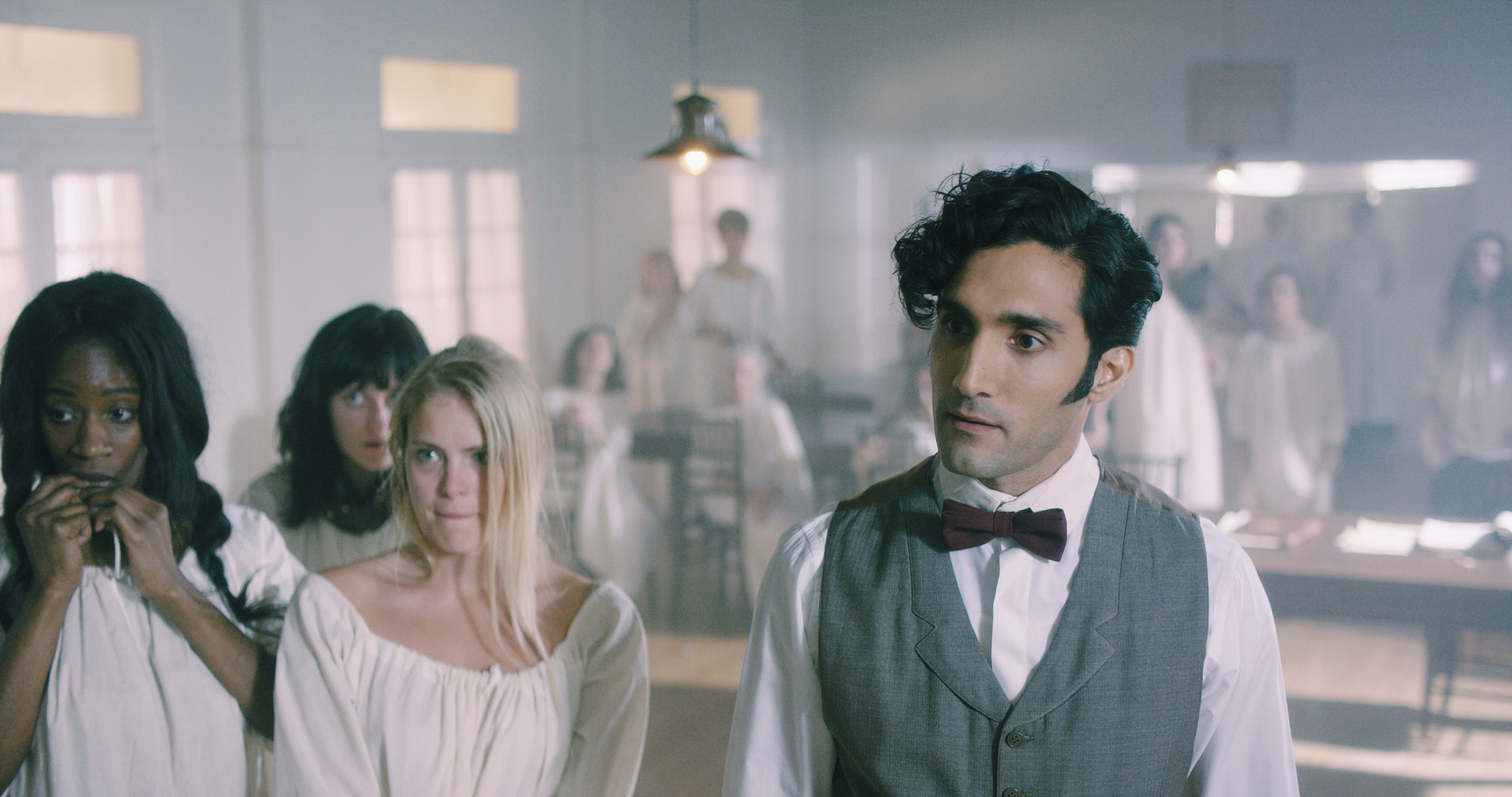 Asylum interior from The Mad Whale, a man in waistcoat and bow tie among patients in white gowns, set decoration by Myra Barrera