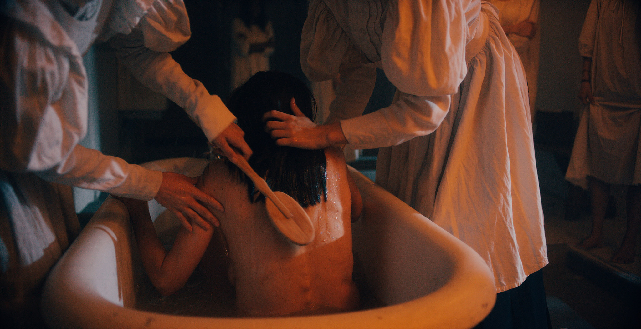 Hydrotherapy bath scene in The Mad Whale, hands over a metal tub in warm orange light
