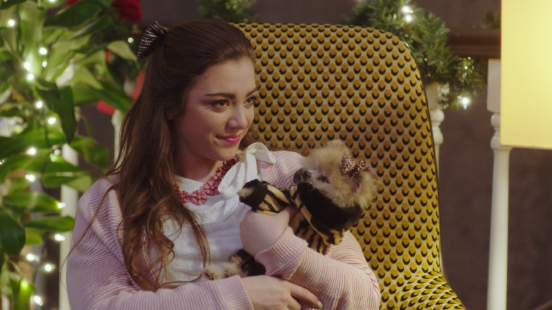 Character in a mustard armchair holding a small dog beside a Christmas tree, This Is Our Christmas